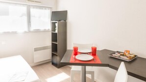A modern, well-lit room with a dining table set for two, a white chair, a small refrigerator, and a window with curtains. - City Rv Sidence Nantes La Chantrerie (Nantes)