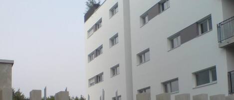 A multi-story building with a flat facade, rectangular windows, and a balcony on the upper floors.