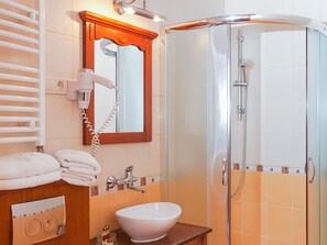 A bathroom with a white sink, a towel rack, a hairdryer, and a glass-enclosed shower.