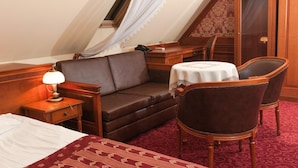 Habitació d'hotel amb un llit, un sofà, una cadira, una taula petita amb una làmpada i una finestra amb cortina.