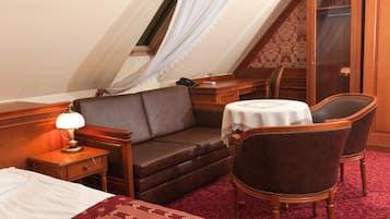 A hotel room with a bed, a sofa, a chair, a small table with a lamp, and a window with a curtain.