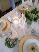 Una mesa puesta para una comida, con platos, cubiertos, una vela y un florero con flores.