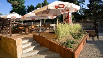 Outdoor seating with white umbrellas labeled 'ŻYWIEC' and a stone staircase leading up to the seating area.