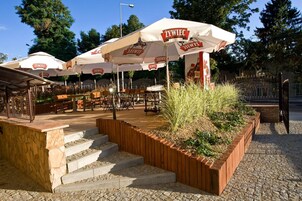 Mesa al aire libre con sombrillas blancas con la leyenda 'ŻYWIEC' y una escalera de piedra que lleva al área de estar.