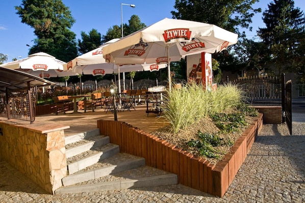 Outdoor seating with white umbrellas labeled 'ŻYWIEC' and a stone staircase leading up to the seating area.