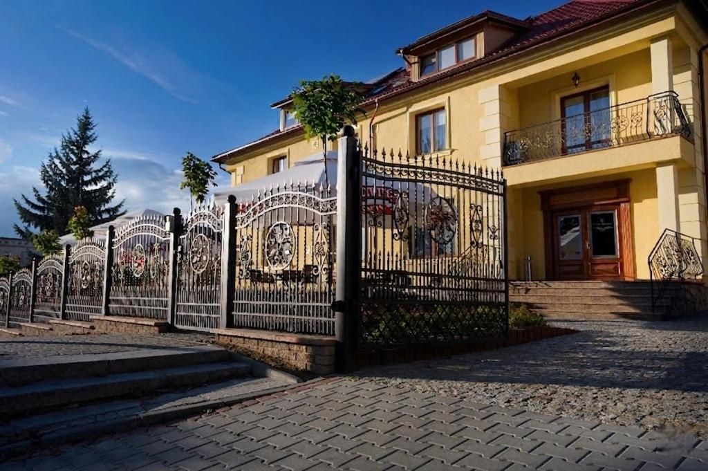A two-story building with a gated entrance, a balcony with decorative railings, and a red-tiled roof.