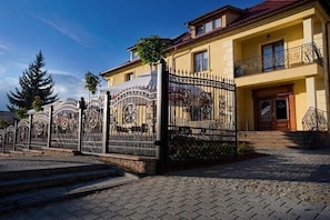 A two-story building with a gated entrance, a balcony with decorative railings, and a red-tiled roof.