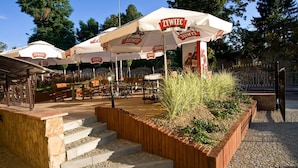 Seients exteriors amb ombrel·les blanques amb la marca 'ŻYWIEC' i una escala de pedra que puja a la zona de seients.