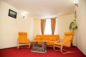 A room with a red carpet, orange furniture, a small table, and a plant.