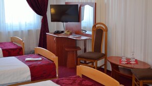 Habitación de hotel con cama, escritorio con televisor, silla, una mesita con un vaso y ventana con cortinas.