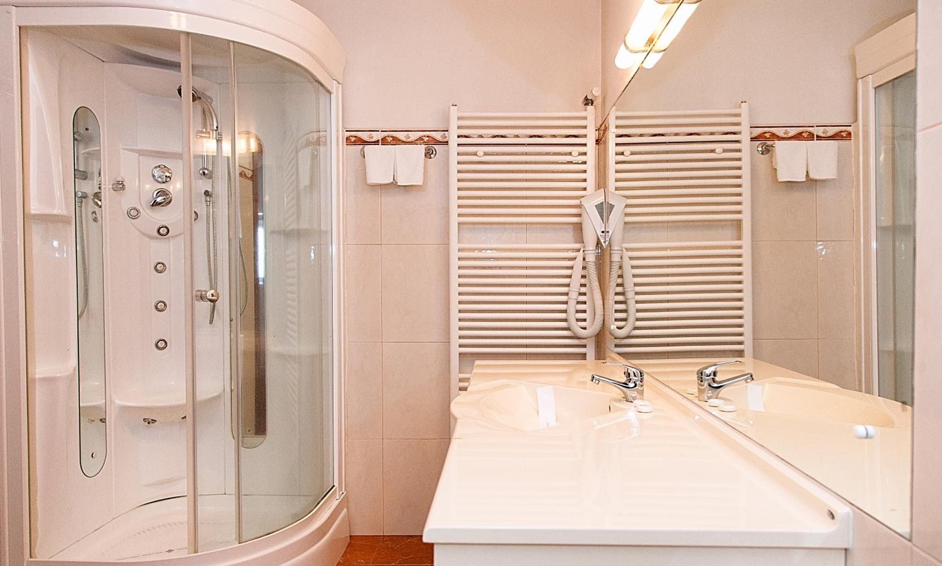 Un baño con ducha envuelta en vidrio, lavamanos doble con espejo y toalleros.