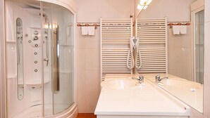 Un baño con ducha envuelta en vidrio, lavamanos doble con espejo y toalleros.