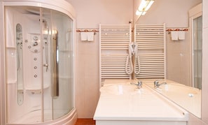 Un baño con ducha envuelta en vidrio, lavamanos doble con espejo y toalleros.