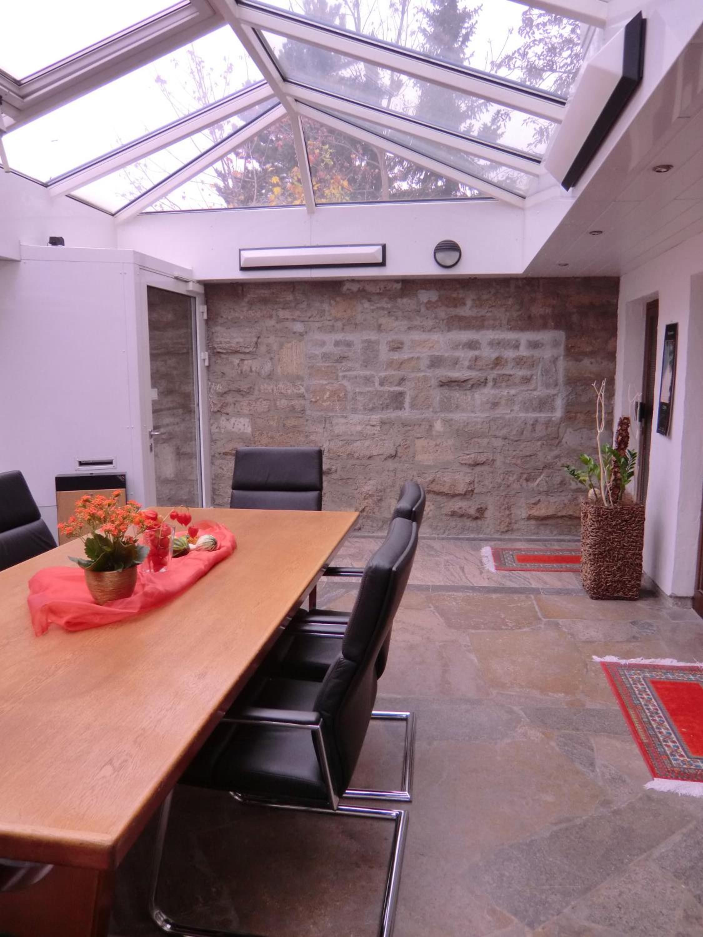 Une salle de conférence avec une longue table, des chaises noires, un mur en pierre et un plafond en verre.