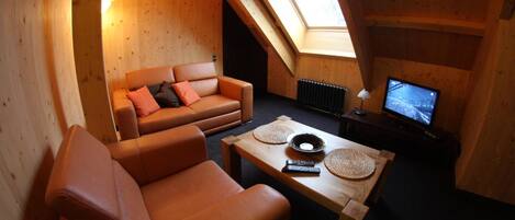 A cozy loft-style room with a wooden interior, a sofa, a coffee table, and a television.