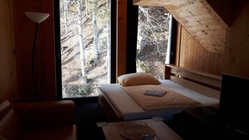 Un dormitorio con cama, mesita de noche, lámpara y vistas a árboles a través de una ventana.