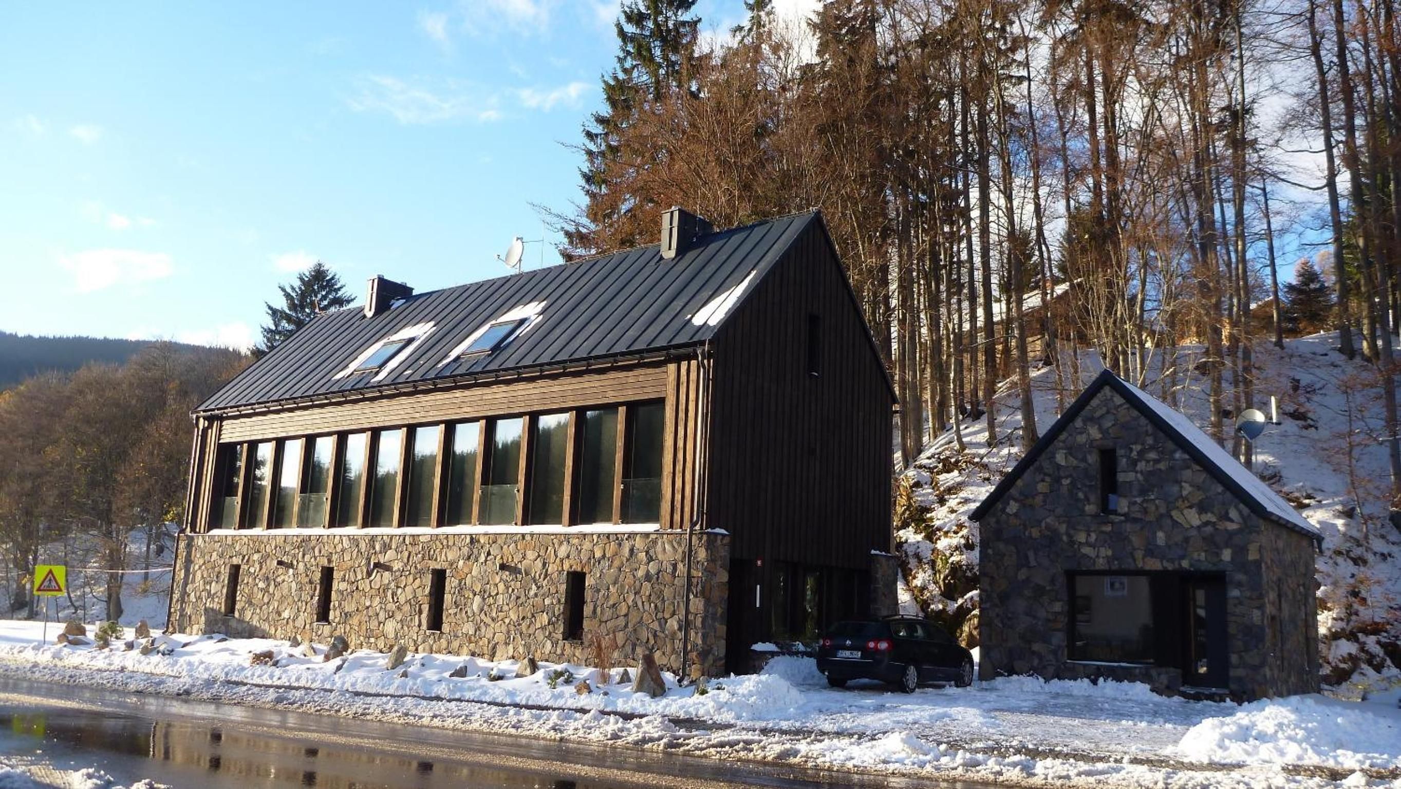 A stone building with a sloped roof, a smaller stone structure attached, and a snow-covered ground.