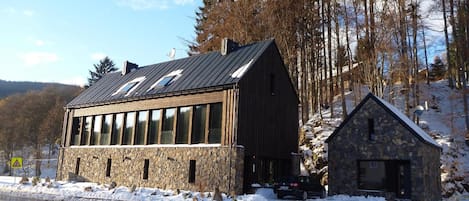 A stone building with a sloped roof, a smaller stone structure attached, and a snow-covered ground.