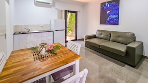 Um espaço compacto com cozinha compacta, mesa de jantar com vela e flores, sofá e uma janela grande com vista para o verde.