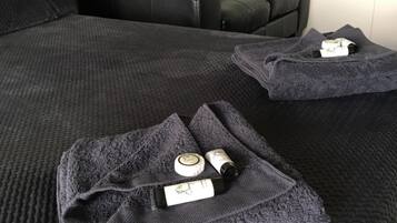 Un lit recouvert d’une couverture texturée de couleur gris foncé, une serviette pliée et une bouteille de lotion posées dessus.