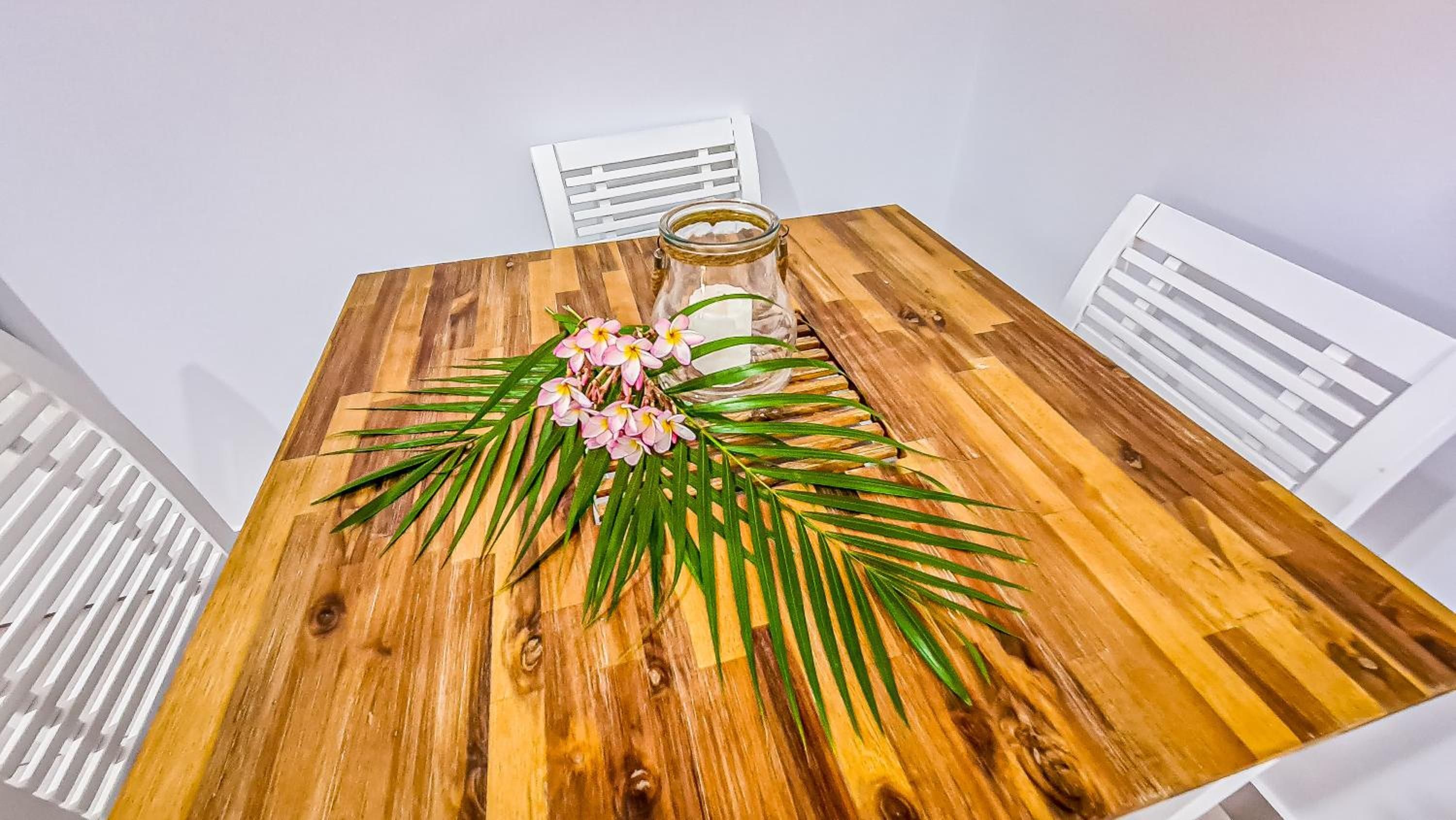 A wooden dining table with a floral centerpiece and a glass jar.