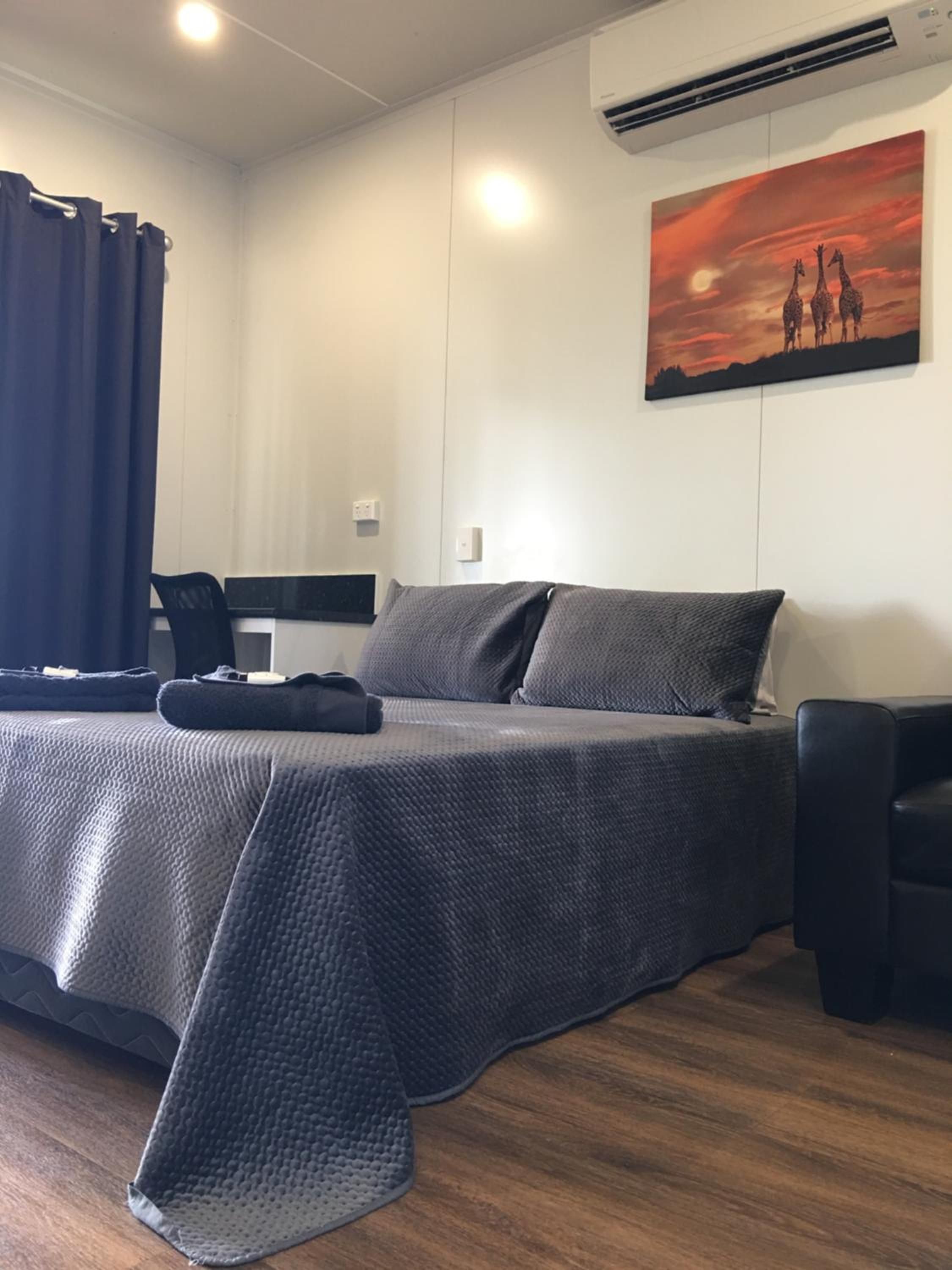A bedroom with a bed, a desk, a chair, and a painting on the wall.