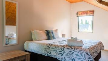 A bedroom with a bed, pillows, a bedside table, a window with a view, and a painting on the wall.