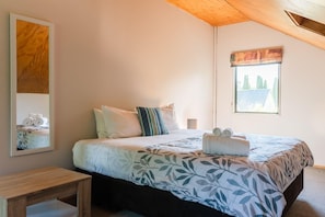Un dormitorio con cama, almohadas, una mesita de noche, ventana con vistas y un cuadro en la pared.