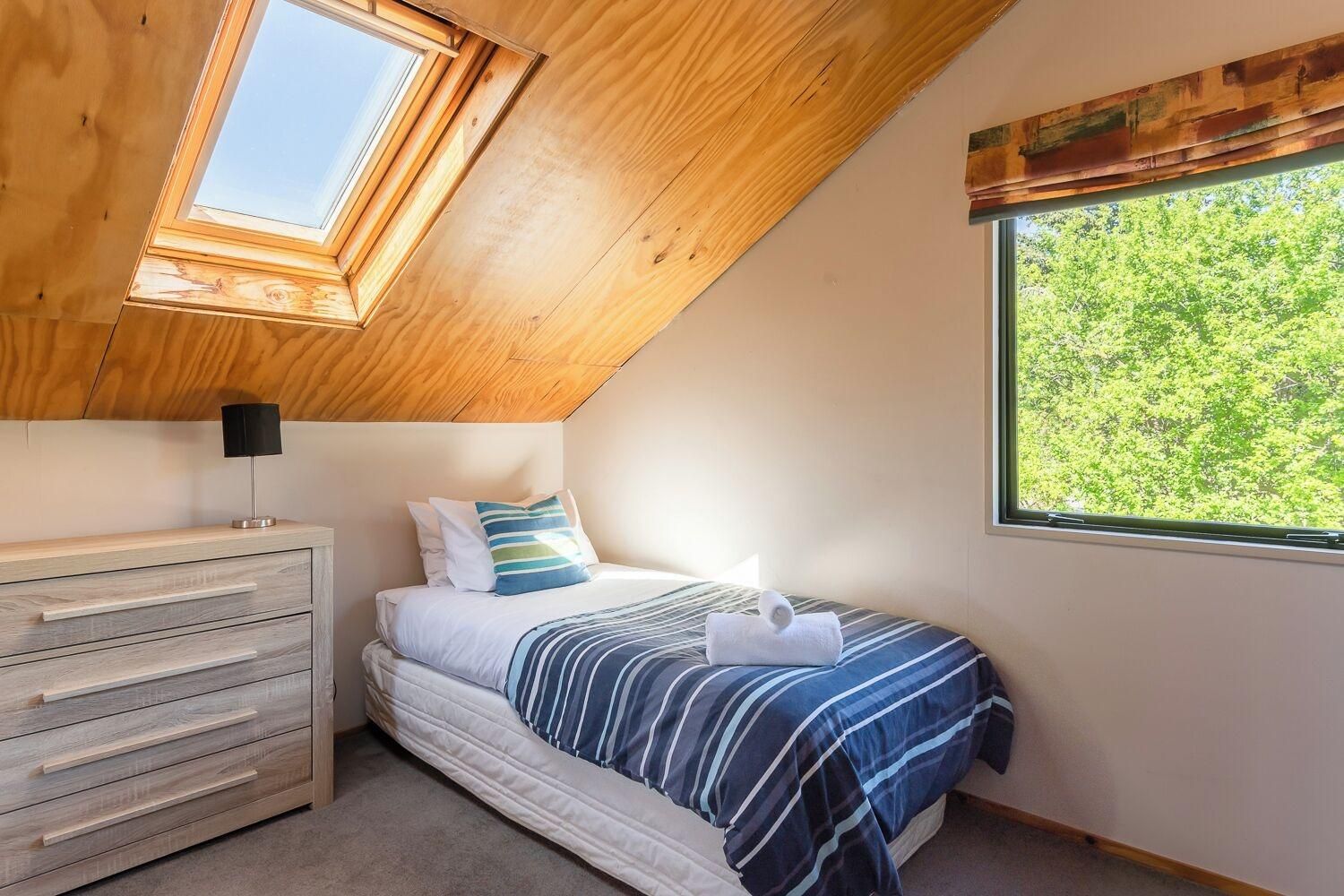 Un dormitorio con tragaluz, una cama con ropa de cama a rayas, una mesita de noche y un aparador.