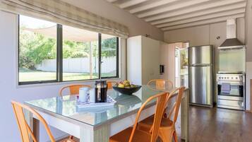 A modern kitchen with a glass dining table, orange chairs, a stainless steel refrigerator, and a built-in oven.