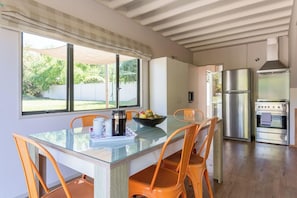 Una cocina moderna con una mesa de comedor de vidrio, sillas naranja, un refrigerador de acero inoxidable y un horno empotrado.