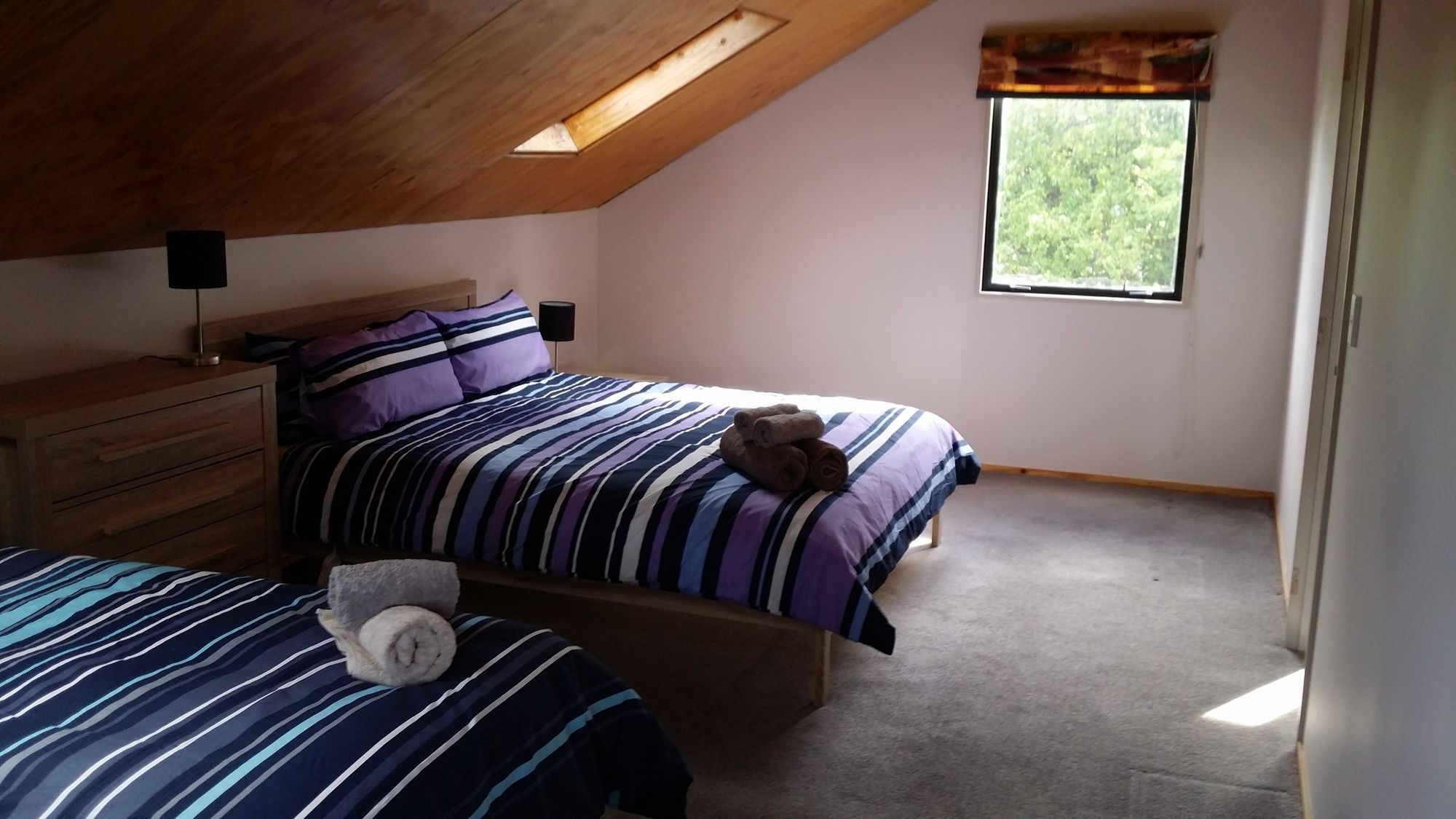 A bedroom with two beds, a wooden dresser, a window with a view, and a skylight.