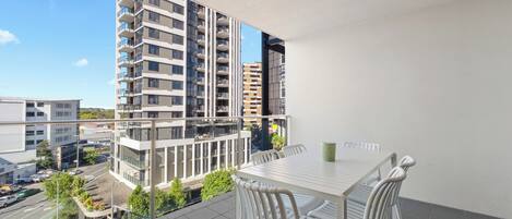 A balcony with a table and chairs, overlooking a cityscape with modern buildings.