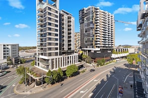 A modern urban street with high-rise buildings, a clear sky, and a bus in the foreground. - Front Row Convenience - Inner City- 3Bed,2Bath,2Car (Woolloongabba)