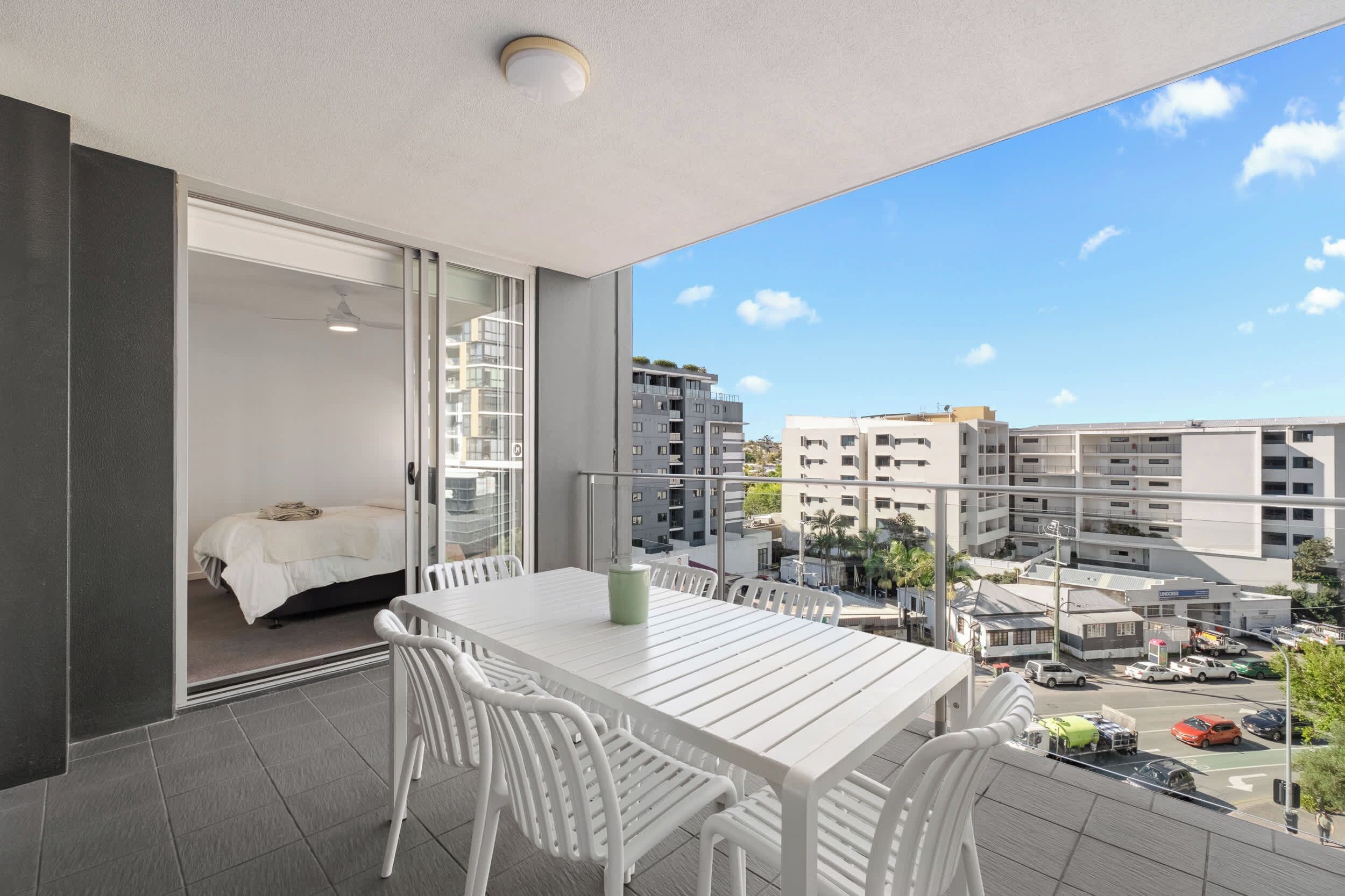 A balcony with a white table and chairs, a bed, and a view of surrounding buildings.
