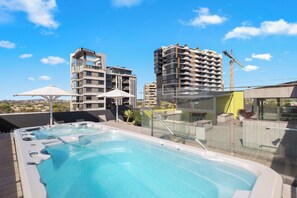 A rooftop pool area with a hot tub, umbrellas, and a view of surrounding buildings. - Front Row Convenience - Inner City- 3Bed,2Bath,2Car (Woolloongabba)