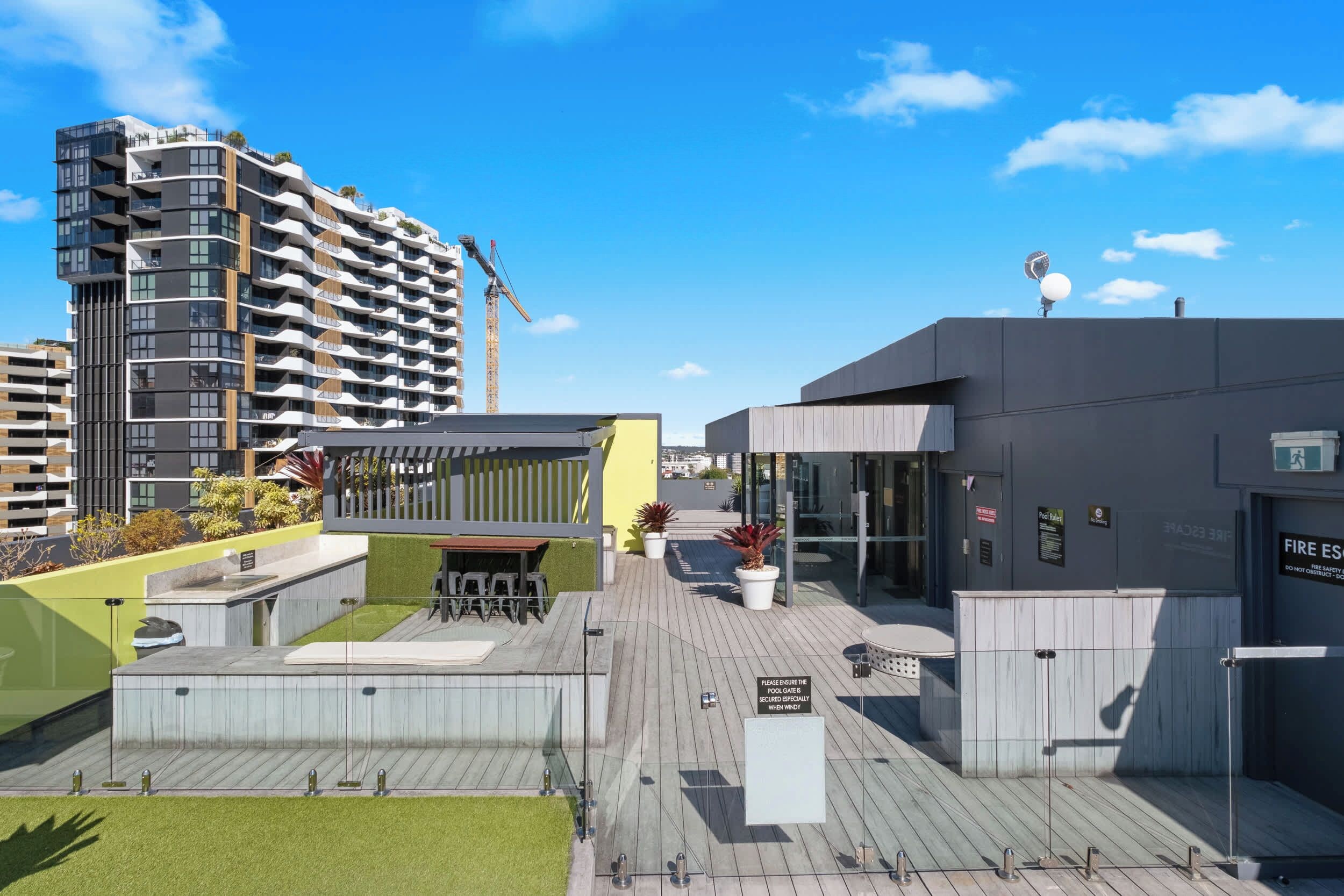 A rooftop pool area with a covered seating area, a pool gate, and a building with a fire safety sign.