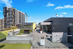 Een dakzwembad met een overdekte zithoek, een zwembadpoort en een gebouw met een brandveiligheidssignet.