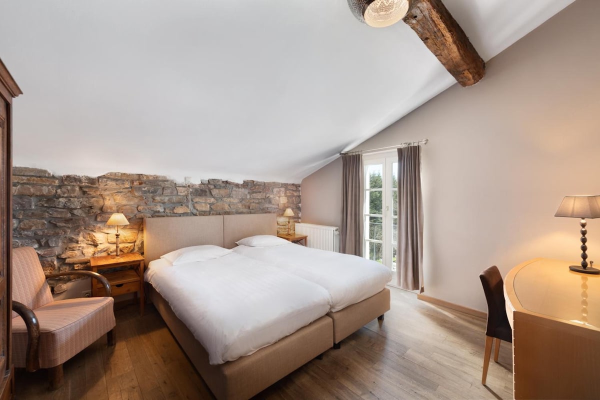 A bedroom with a stone wall, a bed, a desk, and a chair.
