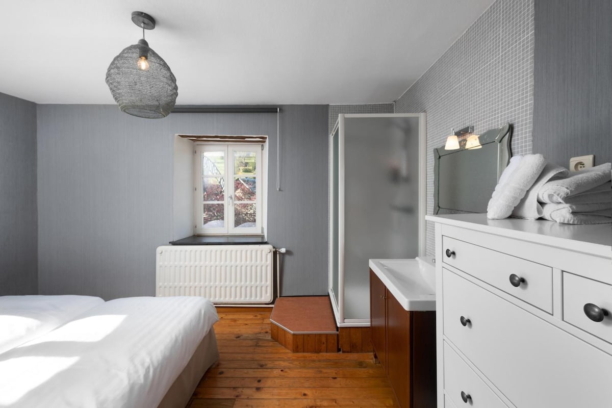 A bedroom with a bed, a dresser, a radiator, and a window.
