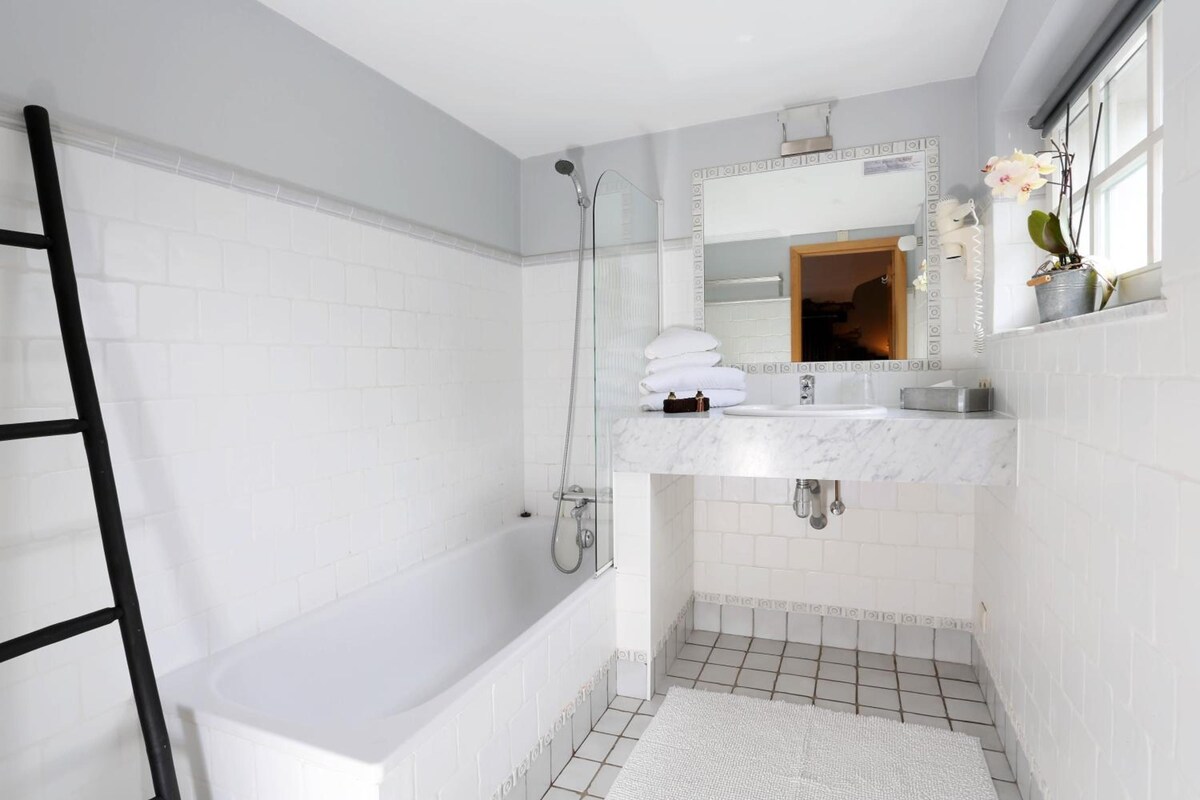 A bathroom with a white bathtub, a shower, a sink with a mirror, and a potted plant.