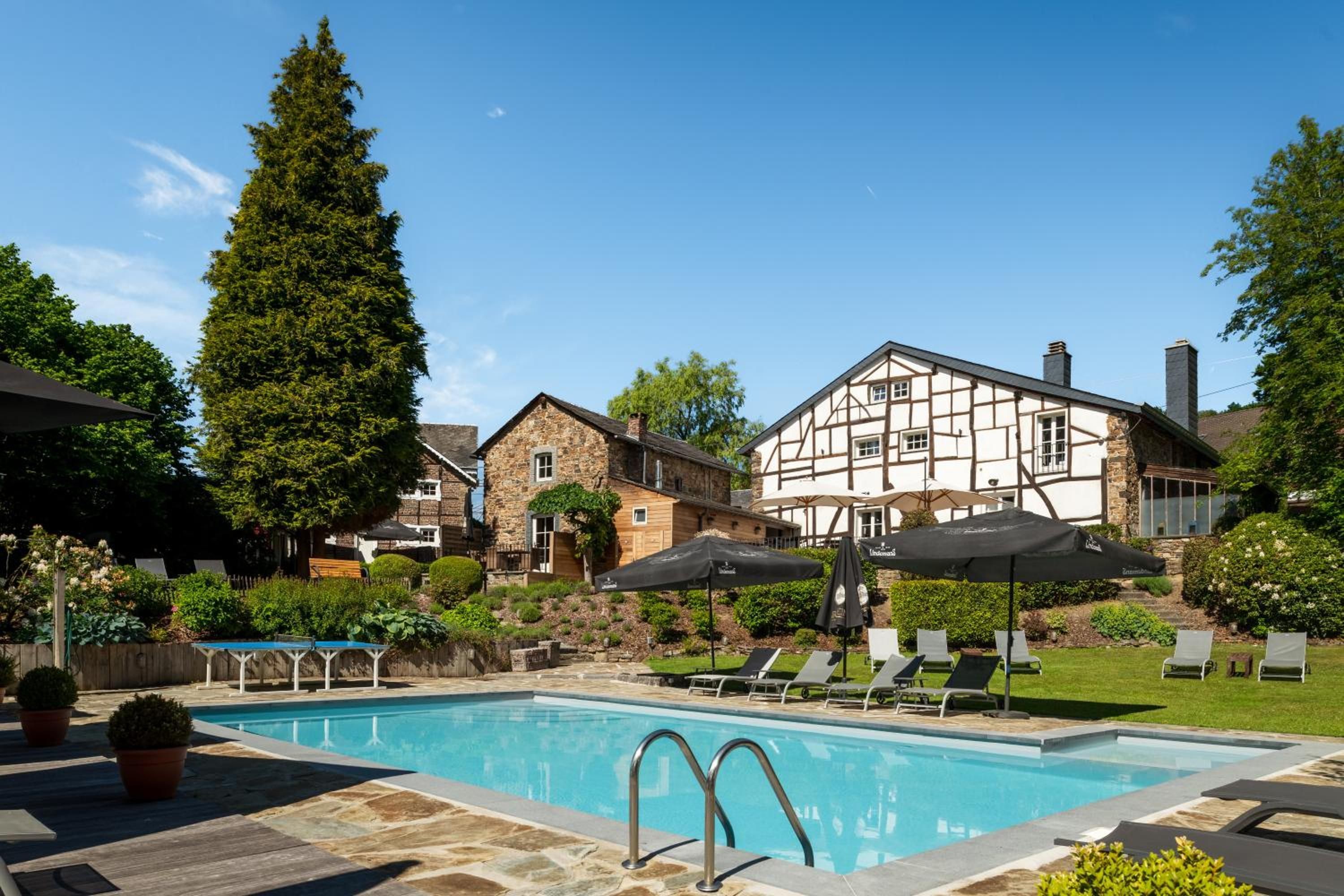 A swimming pool with lounge chairs and umbrellas, surrounded by stone buildings and greenery.