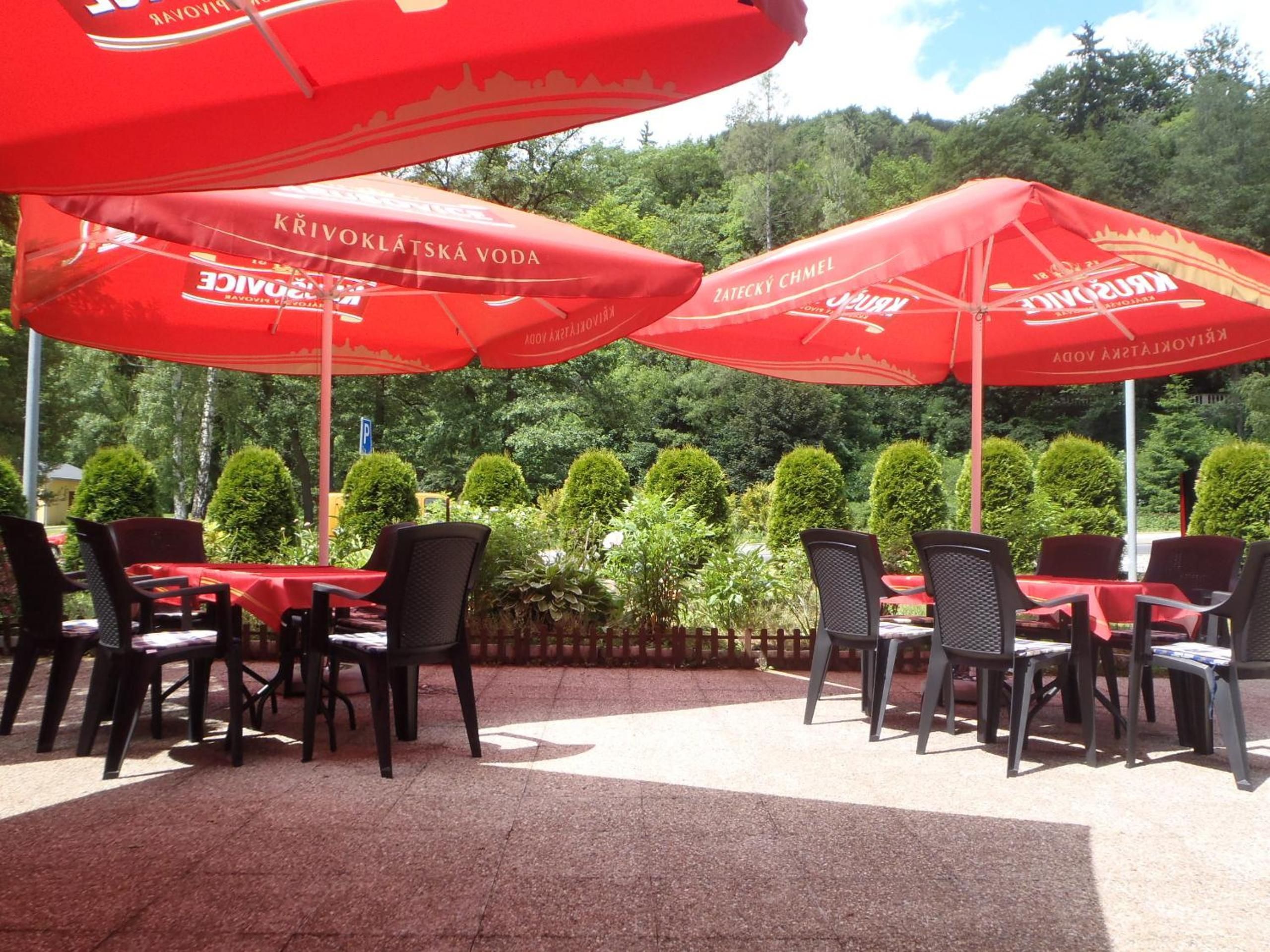 An outdoor seating area with red umbrellas and tables, surrounded by greenery.