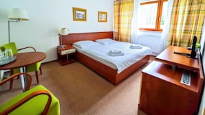 A hotel room with a bed, bedside table, lamp, chair, and a desk with a computer. - Hotel Bazant (Karlovy Vary)