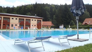 A swimming pool with lounge chairs and umbrellas, surrounded by a building and trees. - Hotel Bazant (Karlovy Vary)