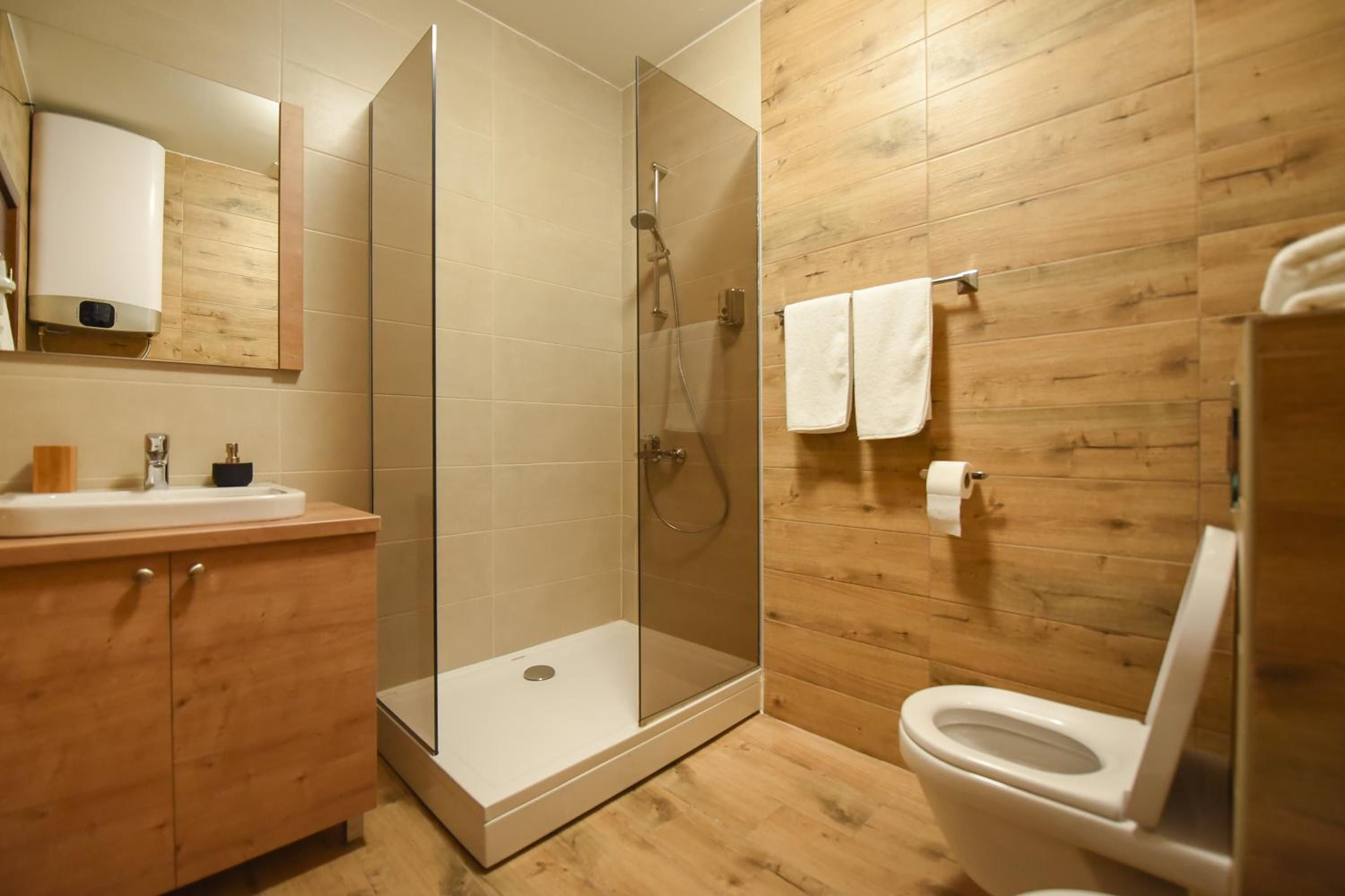 A modern bathroom with a glass-enclosed shower, wooden wall paneling, a white toilet, and a wooden vanity with a sink.