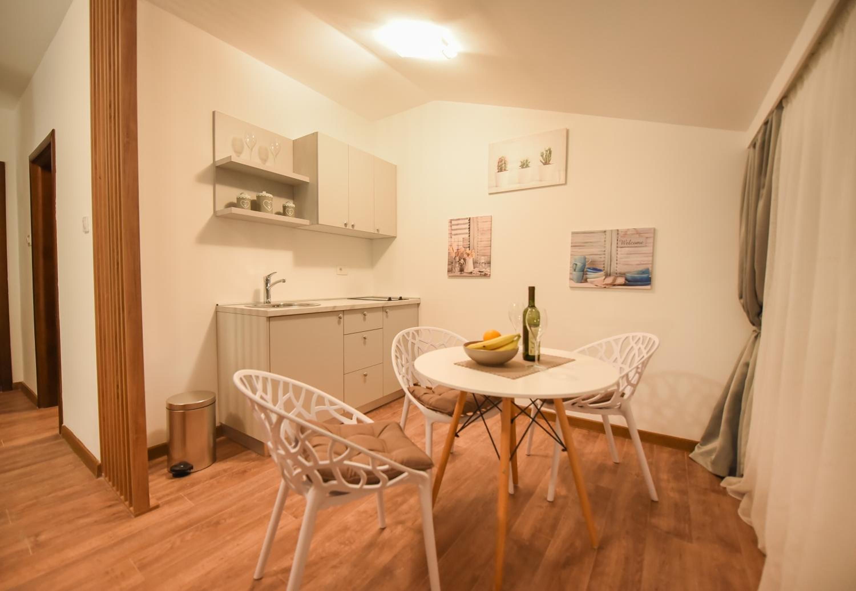A small dining area with a round table, two chairs, a bottle of wine, and a bowl of fruit.