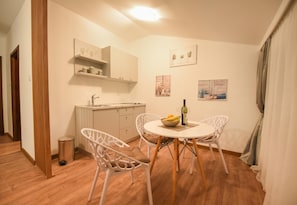 A small dining area with a round table, two chairs, a bottle of wine, and a bowl of fruit. - Korzo Apartmani (Podgorica)