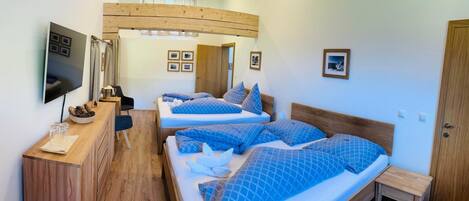 A hotel room with two beds, a wooden desk, a television, and framed pictures on the wall.