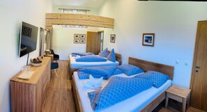 Ett hotellrum med två sängar, ett skrivbord i trä, en tv och inramade tavlor på väggen.